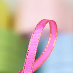 Close-up detail of pink satin ribbon with gold edge for gift packaging and bow making.