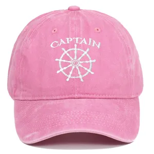 Close-up of white Captain embroidery and ship wheel logo on a pink washed cotton baseball cap
