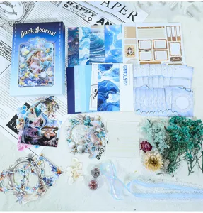 Blauwe junk journal knutselset met achtergrondpapier, stickers, droogbloemen en doos.