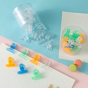 Clear acrylic paper clips and binder clips in storage containers displayed on grid paper.