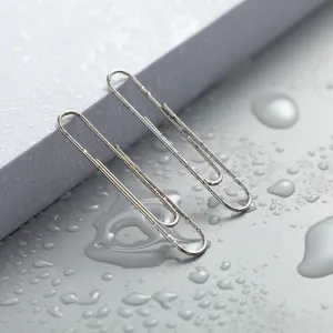 Close up view of long metallic paperclips on wet grey surface, detailed office stationery shot.