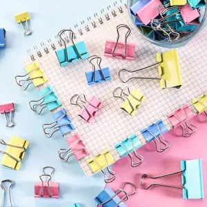 Detailed close-up of colorful metal binder clips in assorted sizes on grid notebook.