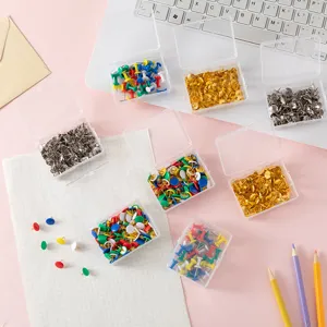 Close-up detail of colorful metal pushpins in clear plastic storage boxes on pink grid desk.