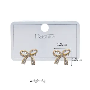 Close-up detail of rhinestone bow stud earrings in gold finish with white display card.