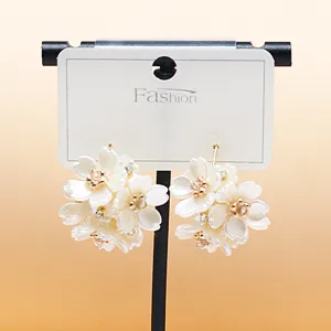 Close-up of white layered floral cluster earrings with sparkling rhinestone centers and gold tone.