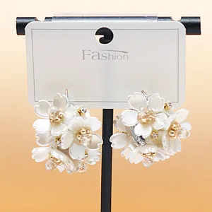 Detailed close-up of white flower cluster earrings with sparkling rhinestones on card stand.