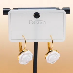Close-up of elegant white rose flower earrings with gold-tone hooks on display card.