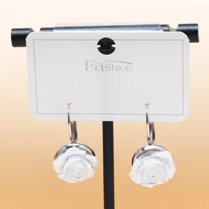 Detailed close-up view of elegant white rose flower drop earrings with silver hooks on card.