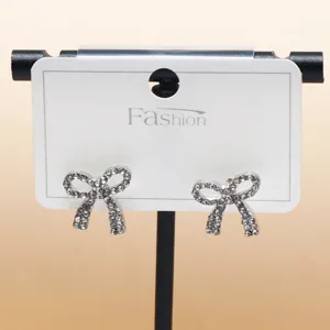 Close-up of sparkling rhinestone bow stud earrings on white display card, elegant jewelry detail.
