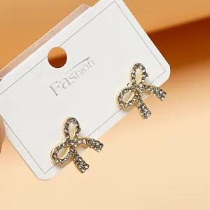 Close up of sparkling rhinestone bow stud earrings on display card, delicate gold metal finish.