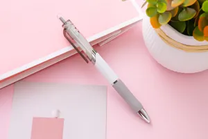 Dettaglio di una penna gel a scatto bianca e grigia su un taccuino rosa chiaro