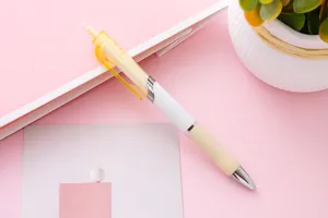 Penna gel a scatto minimalista bianca e giallo crema posata su uno sfondo scrivania rosa