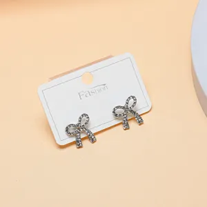 Close-up detail of sparkling rhinestone bow earrings displayed on a clean white card.