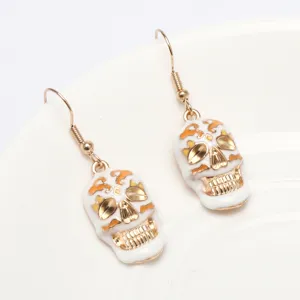 Halloween skull earrings featuring gold tone hooks and white enamel charms for festival.