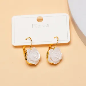 Gold leverback earrings featuring carved white floral pendants on a display card, detailed shot.