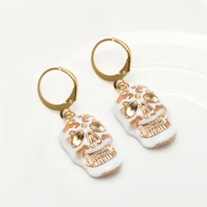 Detail shot of white and gold skull earrings featuring enamel finish and leverback design.