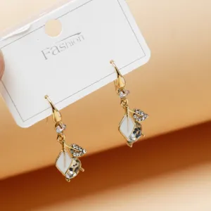Close-up detail of gold-plated drop earrings with white enamel leaves and sparkling crystals.