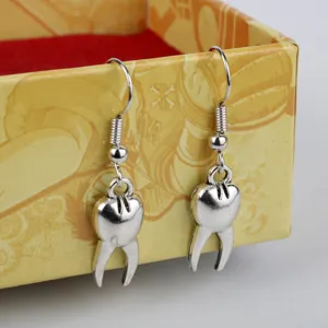Close-up of creative tooth shaped metal hook earrings, quirky silver tone dental jewelry detail.