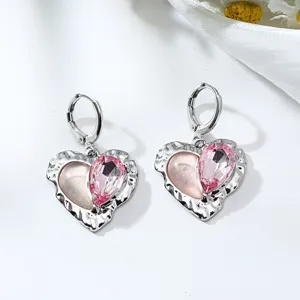 Close-up detail of silver heart-shaped alloy earrings with pink crystal and sweet design.