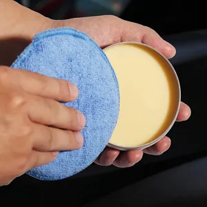 Close-up detail of car wax paste in a round metal tin with a blue microfiber pad.