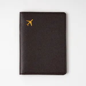 Close-up detail of dark brown PVC leather passport cover with golden airplane stamp motif.