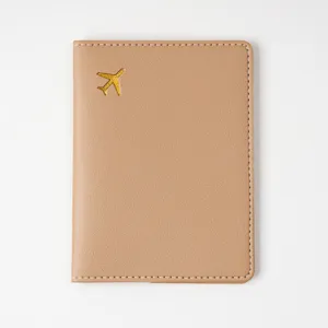 Beige leather passport cover with gold airplane stamp and white edge stitching travel holder