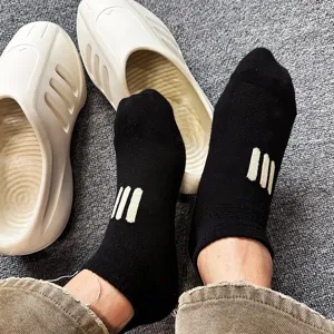 Close-up detail of black ankle socks with three stripes pattern paired with slip-on slides.