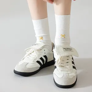 Detail shot of white women's mid-calf socks with yellow bow embroidery and fashion sneakers.