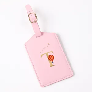 Pink leather luggage tag detail with gold letter T, hot air balloon graphic, and adjustable strap.