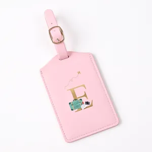 Close up view of a pink leather luggage tag featuring a gold letter E and travel design.