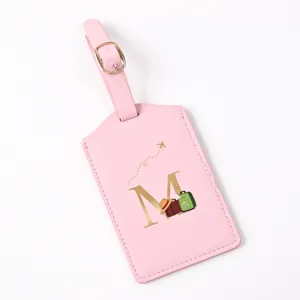Pink leather luggage tag with gold letter M and airplane detail, perfect for travel bags.