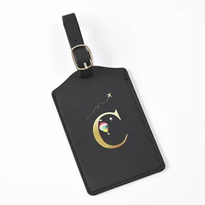 Close-up detail view of black leather luggage tag featuring gold letter C design and buckle strap.