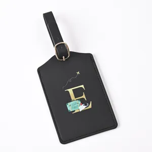 Detailed view of a black leather luggage tag featuring a gold letter E and travel motif.
