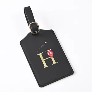 Black leather luggage tag detail, featuring gold letter H and hot air balloon design.