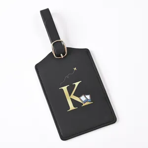 Close-up detail shot of black leather travel luggage tag featuring elegant gold letter K print.