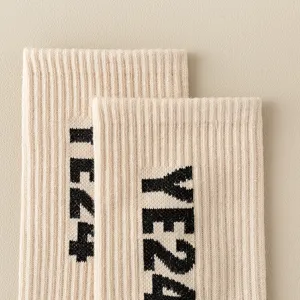 Close-up detail shot of beige ribbed knit long socks with black letter print design.