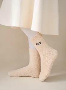 Detailed view of cozy beige fluffy plush mid-calf socks featuring cute embroidered lettering details.