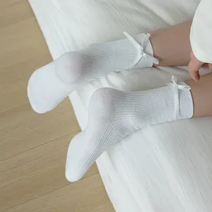 Close-up detail shot of white mid-calf slouch socks featuring delicate ribbon bow accents.