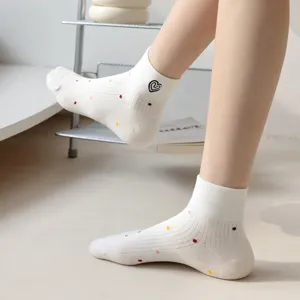 Dettaglio di calzini corti in cotone bianco con pois colorati e un ricamo a forma di cuore.