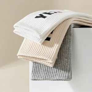 Detail view of stacked high tube knitted socks in white, beige, and grey with letter patterns.