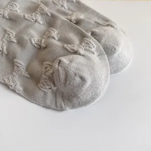 Close-up detail of grey cotton socks featuring an all-over embossed bow pattern for women.