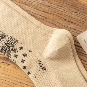 Close-up detail shot of beige cotton socks featuring a classic black paisley pattern.
