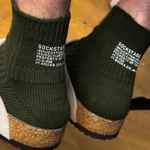 Close-up of green ribbed knit socks with white letter print detail worn with sandals.