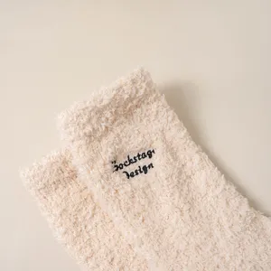 Beige fuzzy slouchy socks with chic black letter embroidery, soft and warm winter wear.