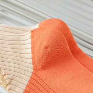 Close-up detail of women's ribbed color-block socks in beige and orange with distressed edge.
