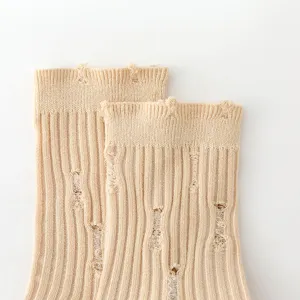 Close-up detail shot of beige knitted ribbed socks with trendy distressed ripped design.