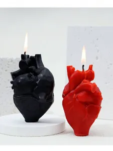 Gros plan de bougies parfumées en forme de cœur anatomique 3D noir et rouge, allumées.