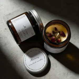 Close-up detail of scented candle in amber glass jar with dried rose petals and silver lid.