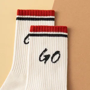 Detailed view of white cotton crew socks with red and black striped cuffs and letter print.