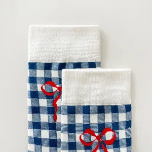 Detailed closeup of blue and white gingham cotton mid-tube socks with cute red bow embroidery.